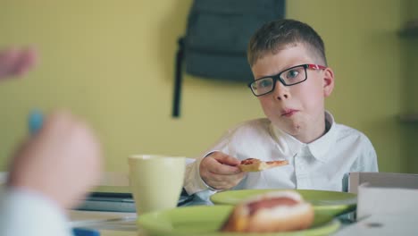 niño come pizza mirando a su compañero de clase con un girador en la mesa