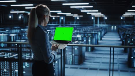 especialista femenina que utiliza la computadora portátil de llave de croma en el centro de datos. gran granja de servidores instalación de computación en la nube con ingeniero de mantenimiento trabajando con computadora de pantalla verde. ancho medio sobre el hombro