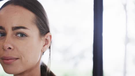 Half-face-of-smiling-biracial-young-woman-against-window-in-yoga-studio