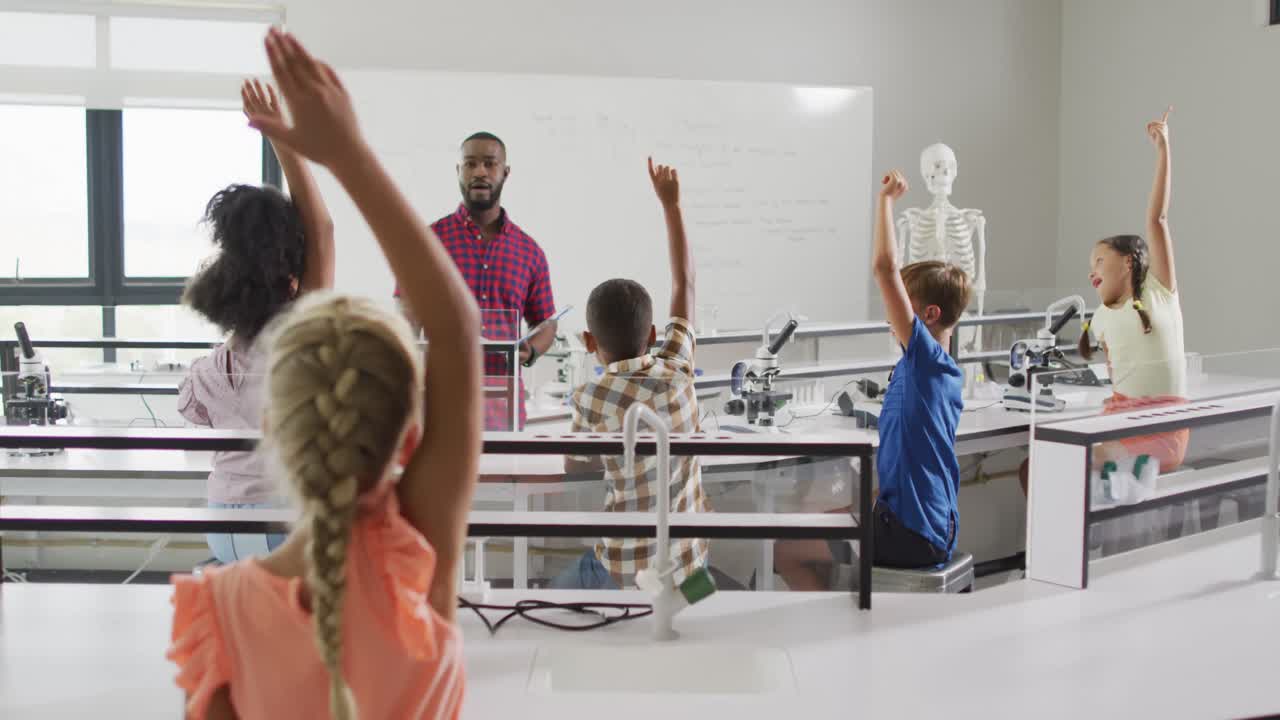 Video of african american male teacher during anatomy lesson and diverse pupils raising hands
