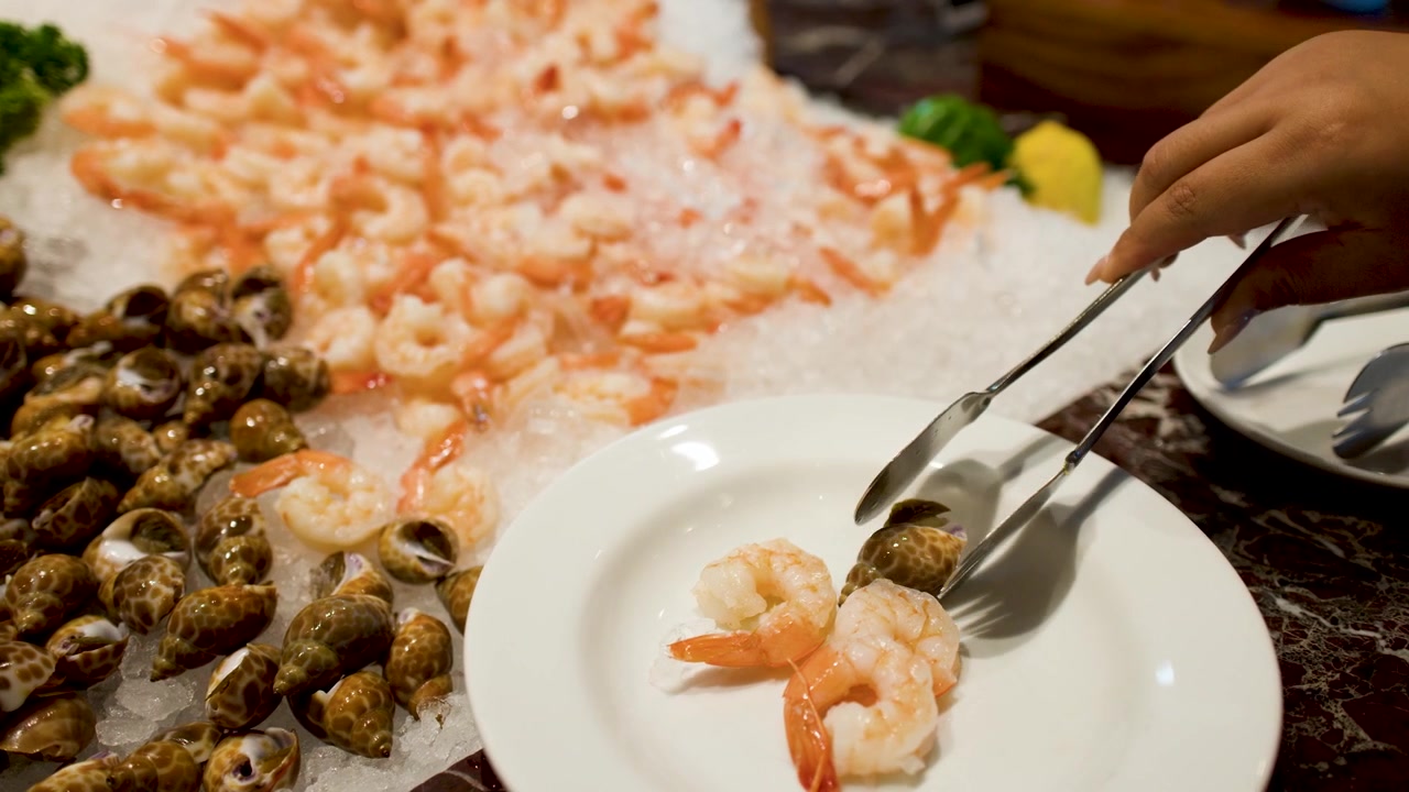 Una mano usa delle pinze metalliche per prendere frutti di mare freschi dal ghiaccio in un ristorante.