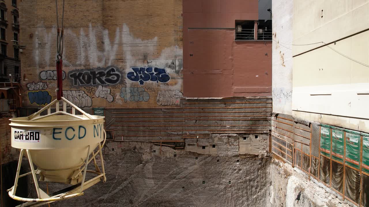 Concrete bucket suspended over a deep urban construction excavation