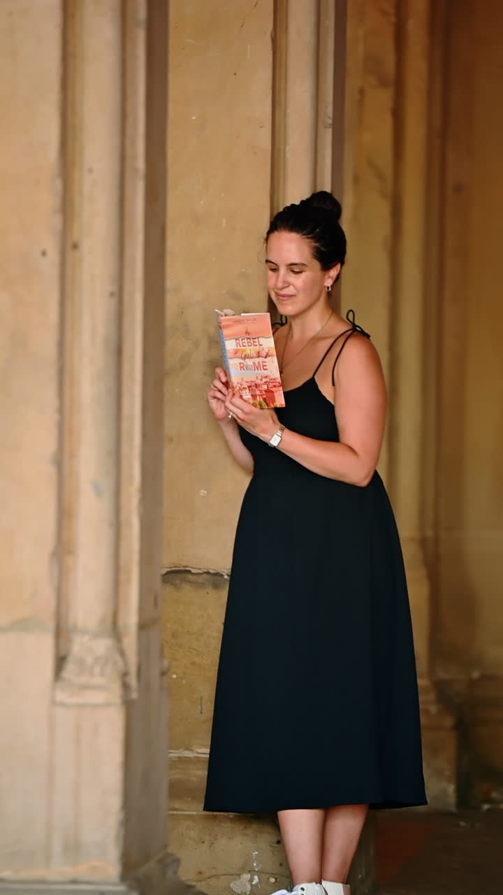 New York, USA, 1 agosto 2025: donna che legge un libro vicino a colonne di pietra. Una donna con un abito nero legge un libro vicino a colonne di pietra a New York
