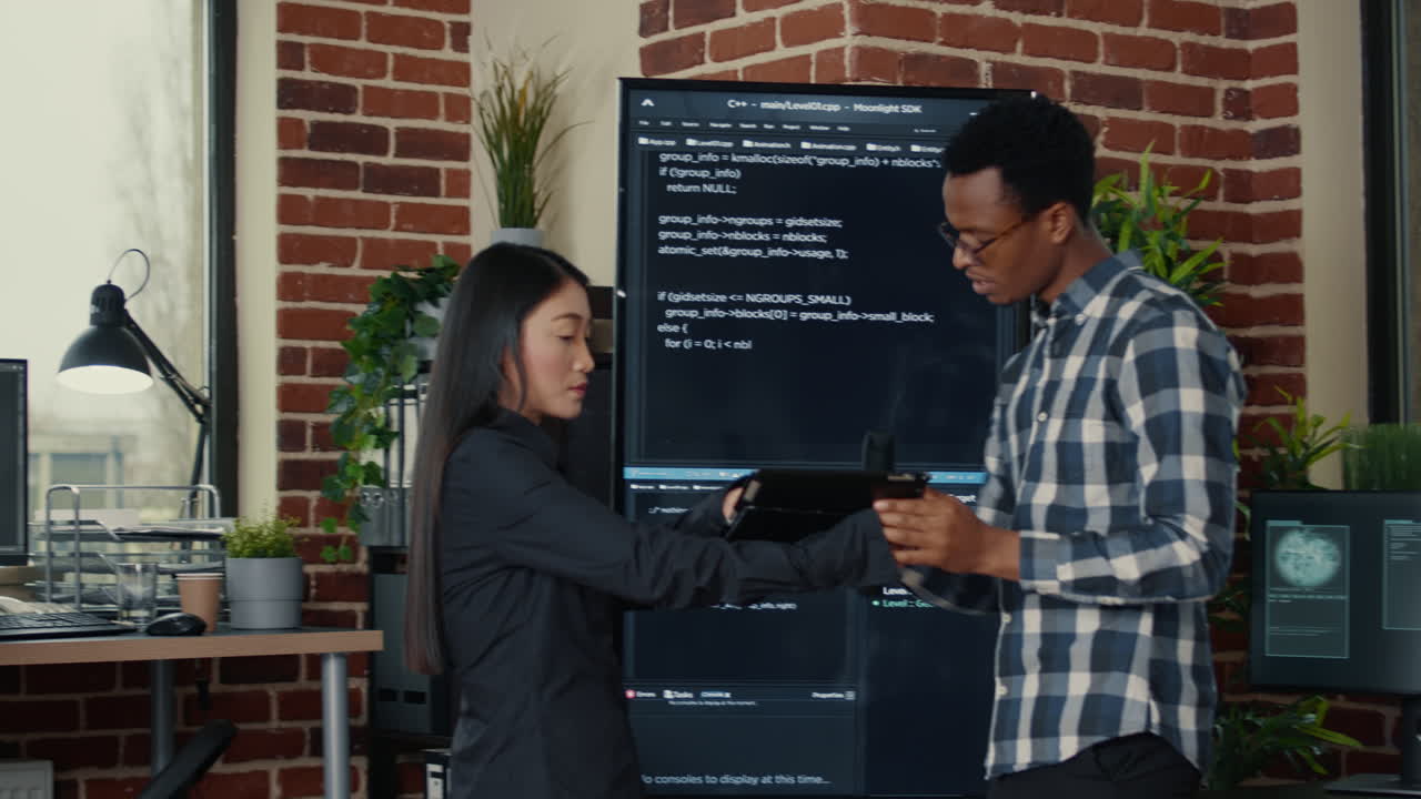 Software engineers analyzing code on wall screen tv comparing errors using digital tablet
