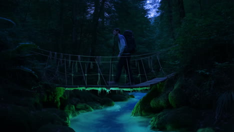 a person crossing a suspension bridge over a stream in a forest