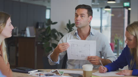 equipo de arquitectos reunidos alrededor de una mesa discutiendo el plan en una oficina moderna de plan abierto