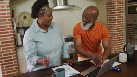 una feliz pareja de ancianos afroamericanos usando una computadora portátil en la cocina de su casa