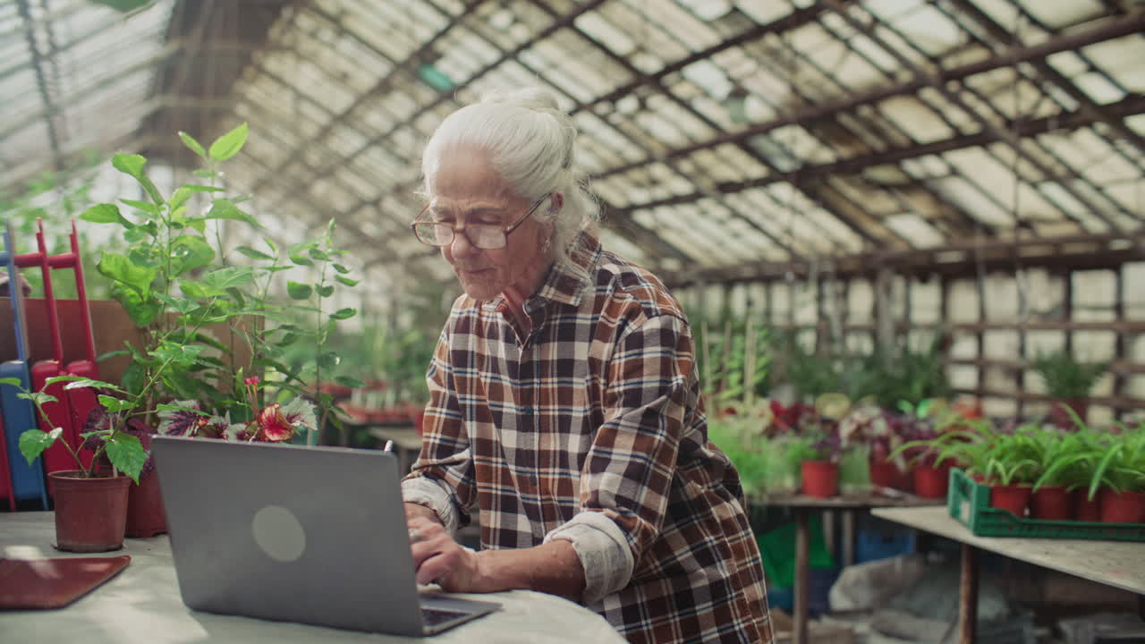 Senior Woman Using Laptop and Writing Notes in Commercial Greenhouse