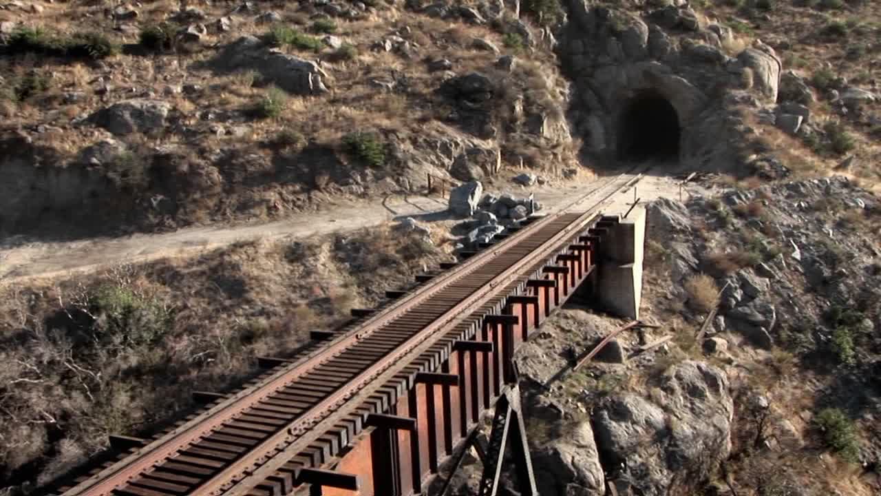 un helicóptero sobrevuela las vías del tren en un puente que conduce a un túnel