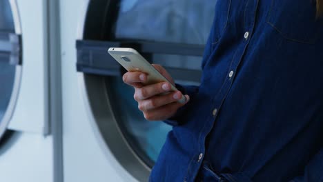 Woman-using-mobile-phone-at-laundromat-4k