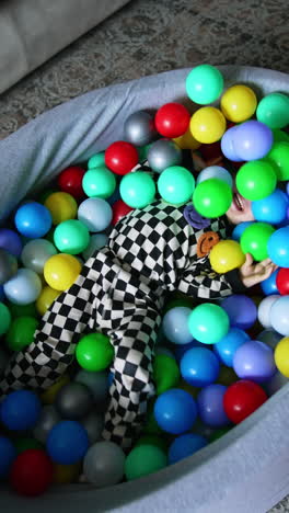 joyful energetic toddler boy tumbles in the dry pool among the colorful balls. happy childhood concept. top view. vertical video.