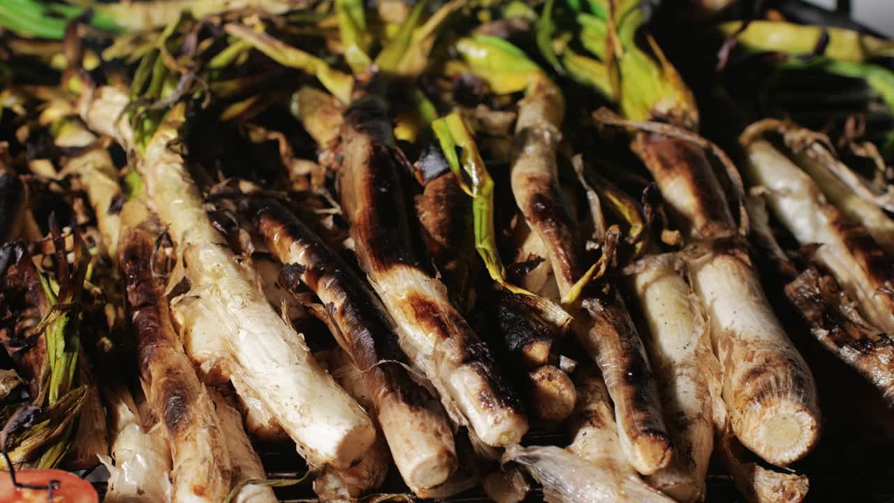 Traditional Spanish catalan green winter onion calcots, spring green season grill barbecue, vegan bbq with fire in Barcelona, Catalonia. Close up of grilling green onion.