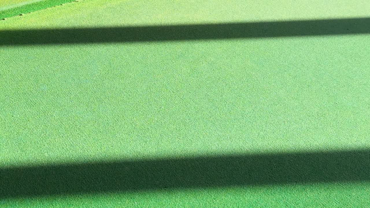 Een gele poolbal beweegt over groen vilt onder helder zonlicht met lange horizontale schaduwen