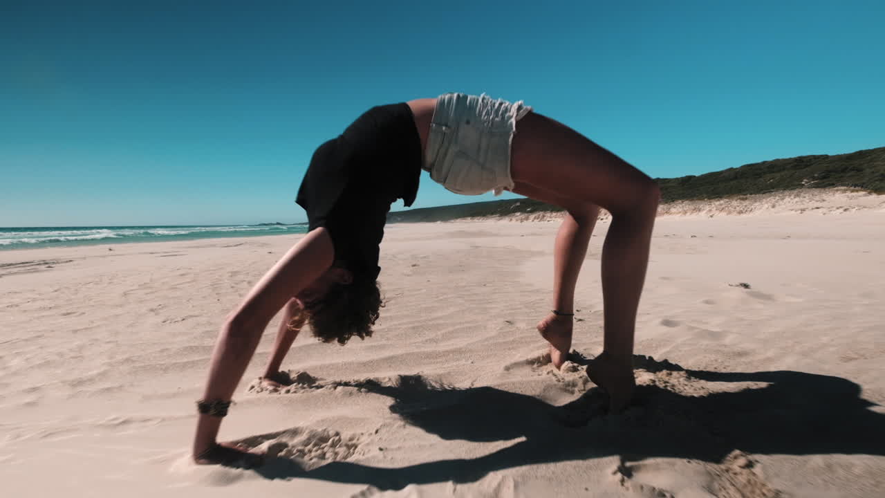 cámara lenta alejar la toma de una chica haciendo ejercicio de puente de yoga en la playa durante el sol