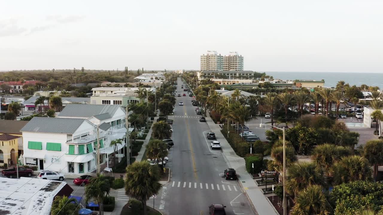 Aerial drone shot of road lined with houses and trees under clear sky in Hawaii. Parked cars add detail to the peaceful neighborhood scene from above.