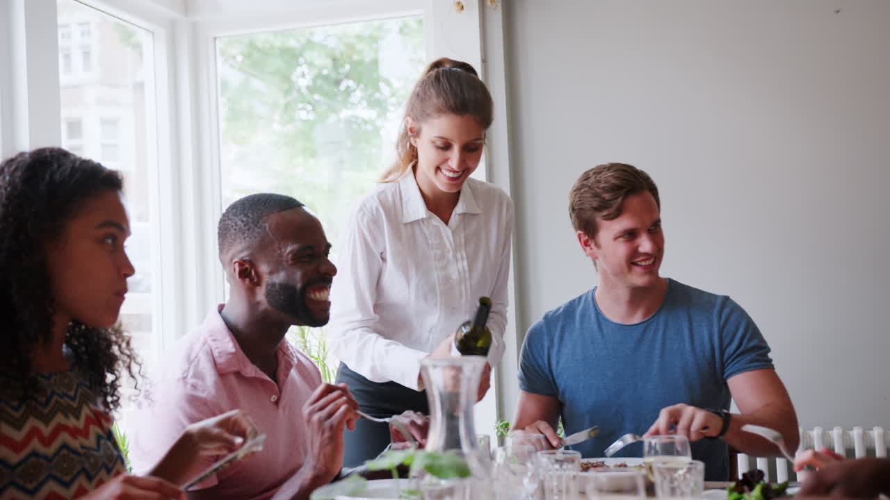 Waitress Serving Wine To Group Of Friends Eating Meal In Restaurant Together