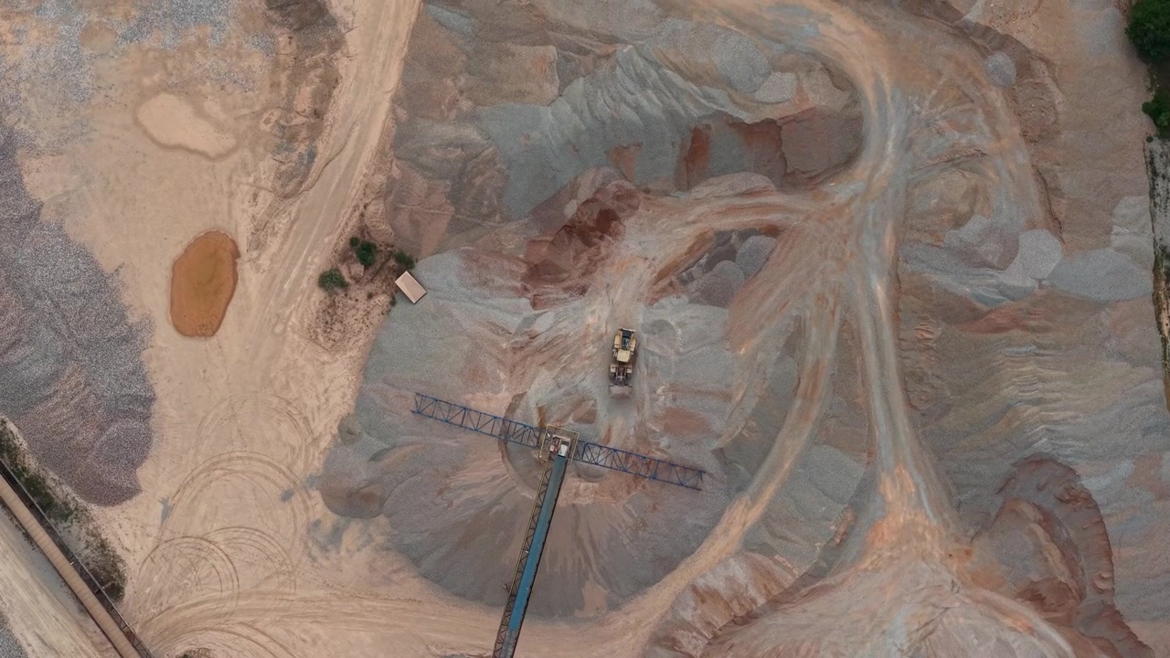 An aerial view reveals an excavator engaged in processing raw aggregates within a sprawling industrial quarry, highlighting resource extraction.