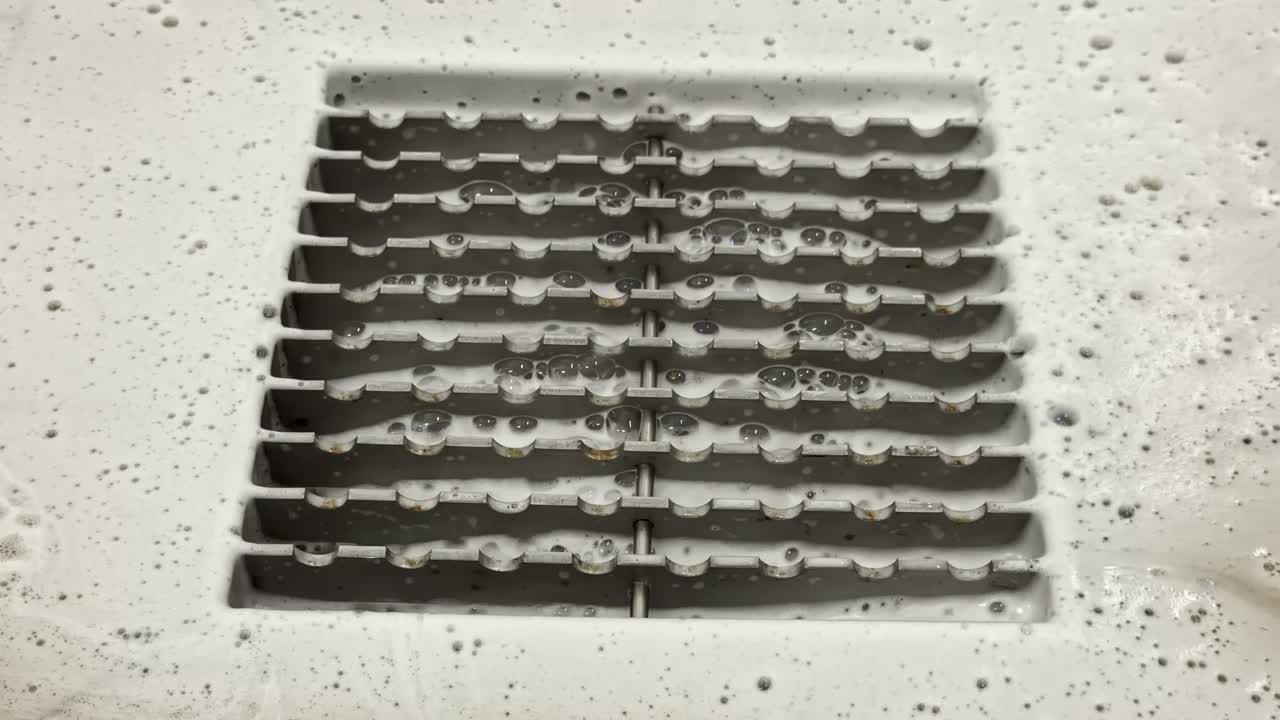 Industrial floor drain grate embedded in concrete surface, closeup as water and bubbles drain