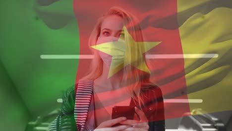 Animation-of-flag-of-cameroon-waving-over-woman-wearing-face-mask-during-covid-19-pandemic