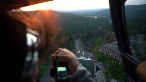 female photographer taking pictures from helicopter cabin during sunset flight