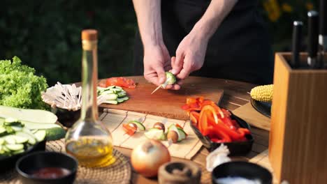 young man preparing vegetable skewers for grilling medium shot