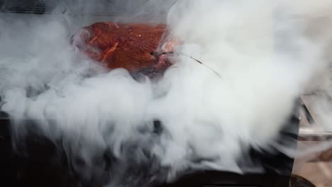 Starker-Rauch-Von-Einem-Pelletgrill-Verdeckt-Das-Schweinefleisch-Auf-Dem-Rost,-Der-Rauch-Lichtet-Sich-Kurzzeitig-Und-Gibt-Den-Blick-Auf-Den-Schweinerücken-Frei