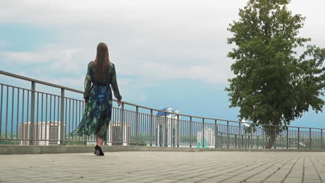 young woman in stylish dress walks along city viewing deck