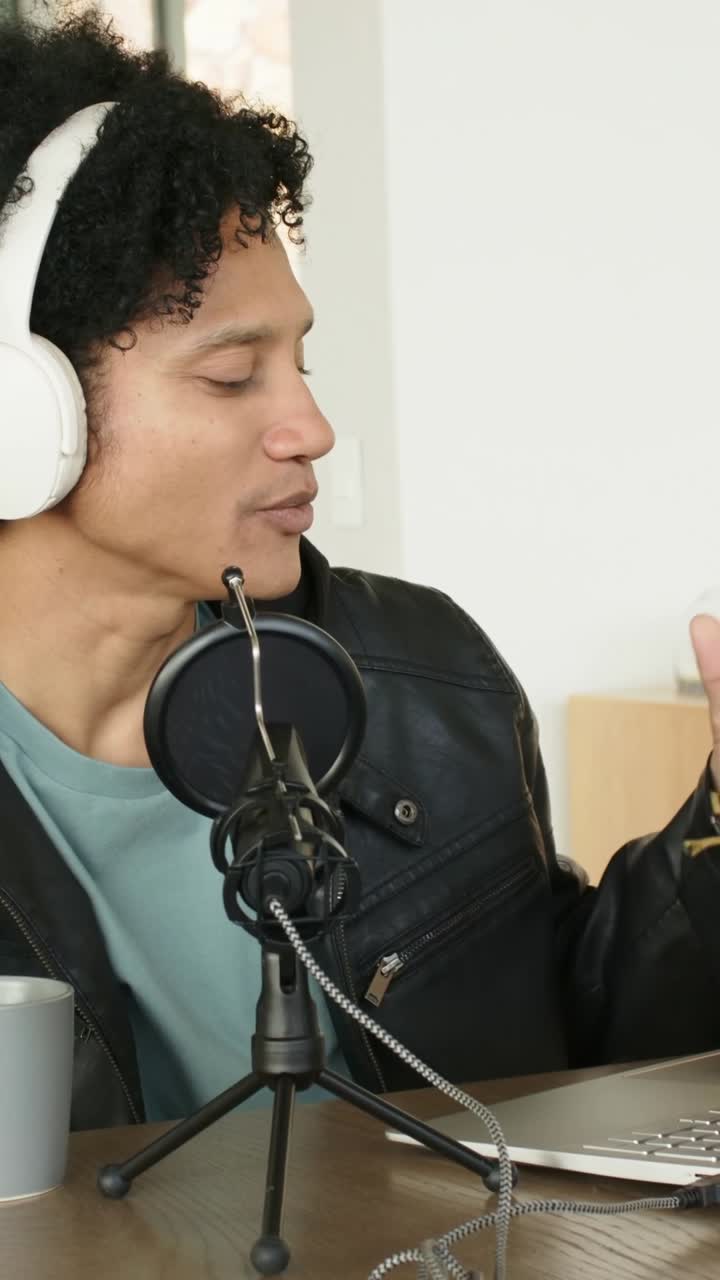 Vertical video: Starting live man in headset and jacket speaking into mic, typing on laptop at home