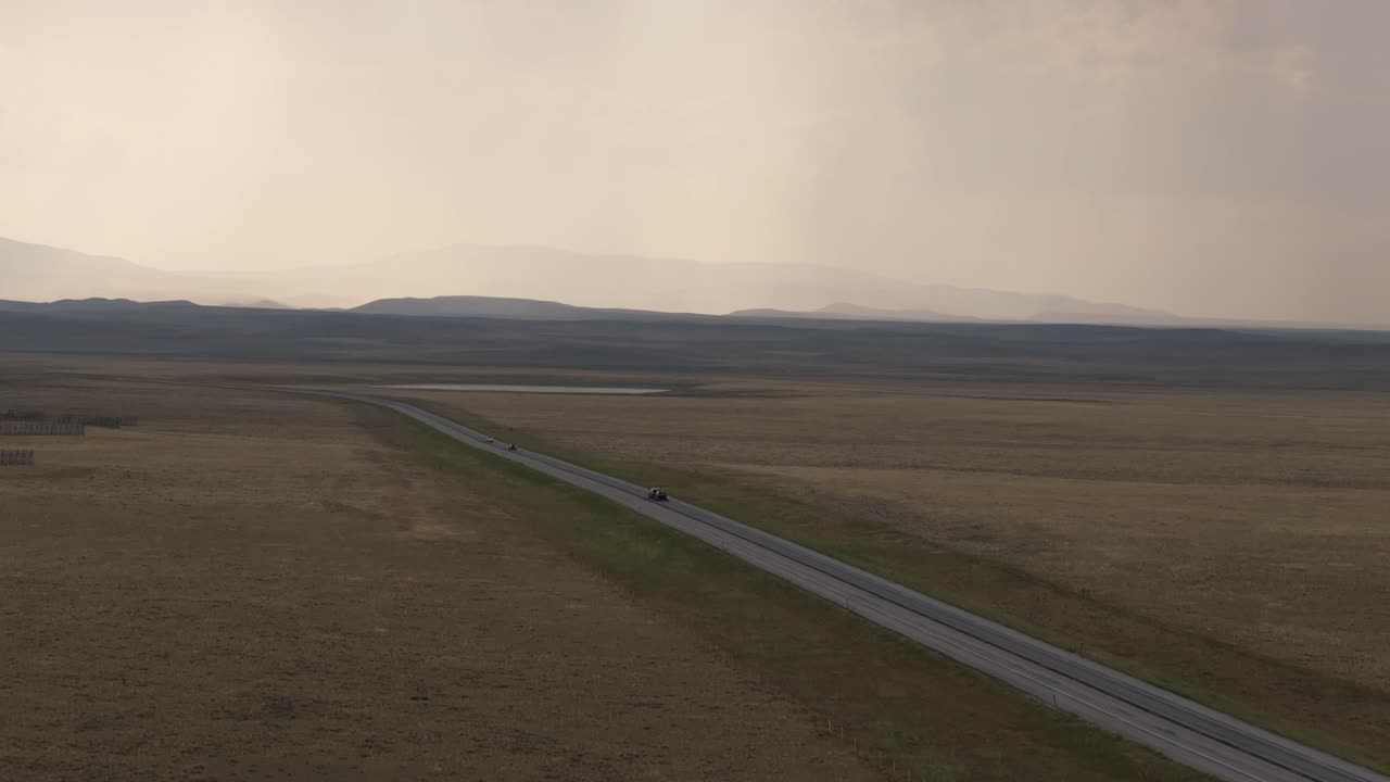 모터사이클은 폭풍우 구름 아래 광활한 중부 와이오밍 풍경에서 긴 고속도로를 따라 이동합니다.