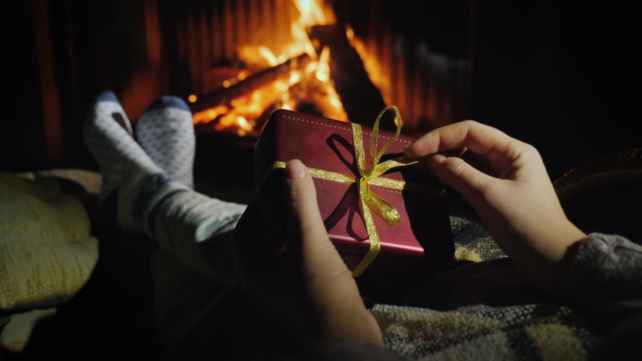 여자는 벽난로 근처에 앉아 손에 선물 상자를 들고 있다