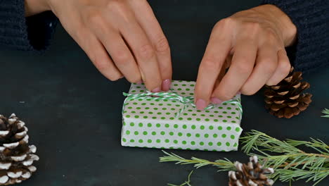 female hands decorate a gift box with green wrapping with a pine branch