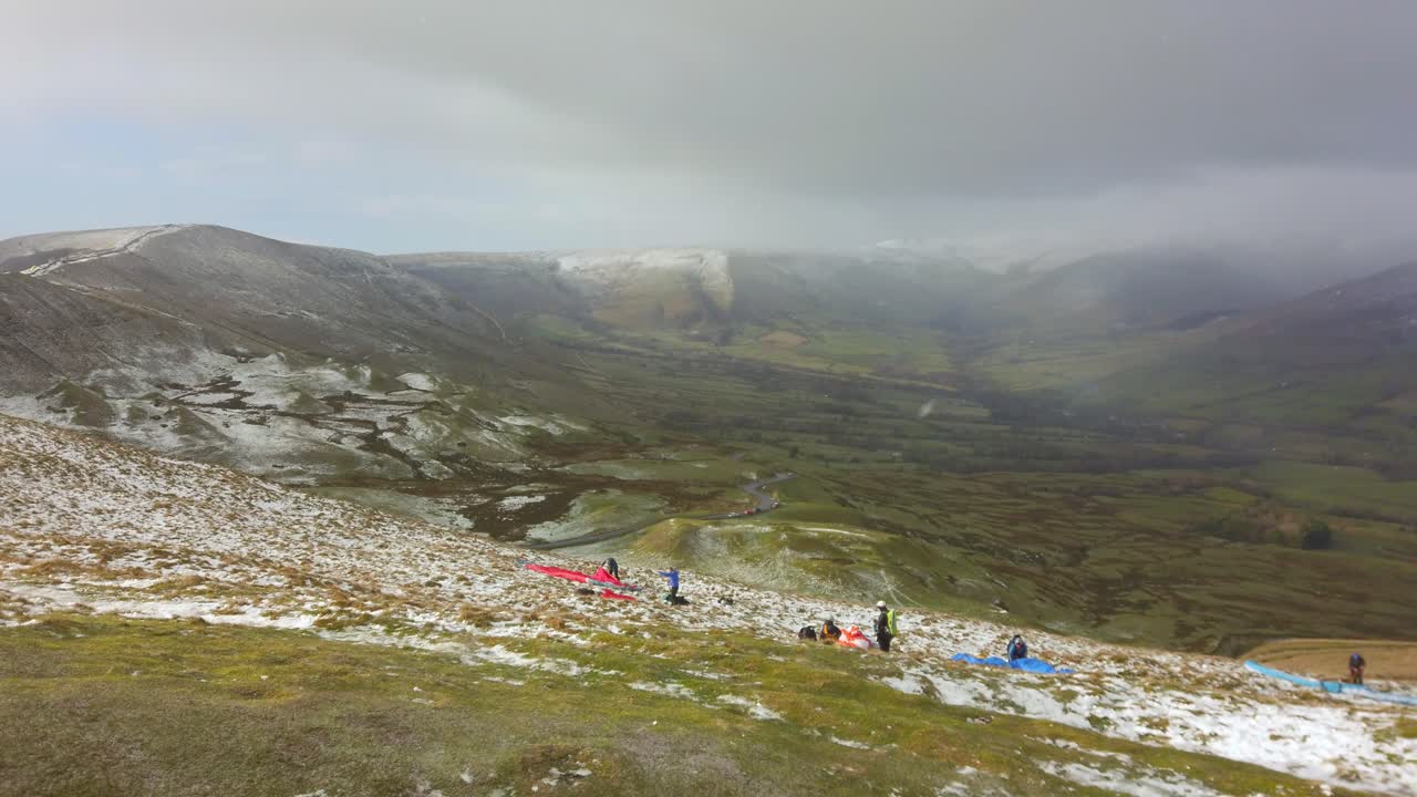 Paragliders setting up for flight on edge of mountain with snow on horizon
