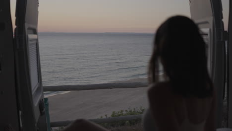 woman watching sunset from a camper van at the beach
