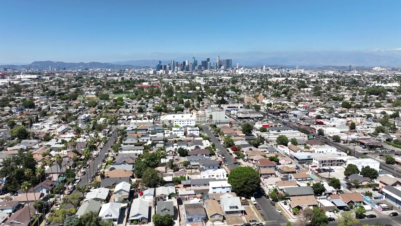 Filmato drone che mostra lo skyline del centro di Los Angeles in lontananza, oltre un vasto quartiere residenziale ricco di numerose case, tetti, strade e un'area urbana.