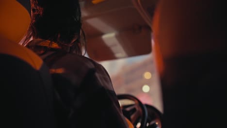 Rear view of a brunette man with long hair in a checkered shirt driving a car in the evening through the city after his work when he goes home. Evening ride around the city