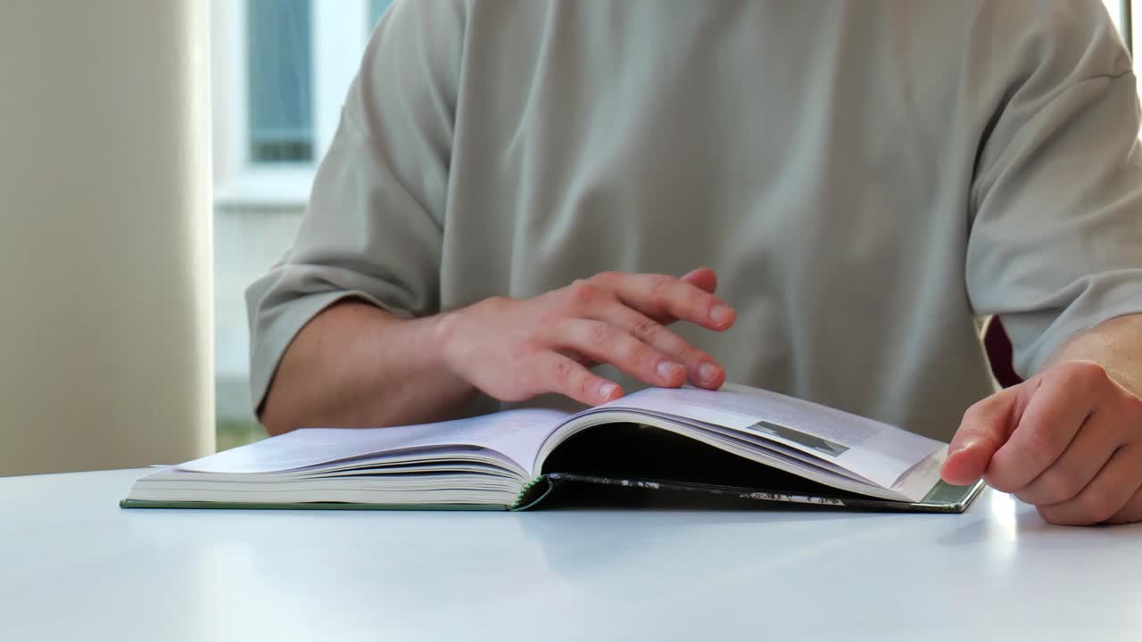 Man sitting on a table and reading a book. Turning pages slowly