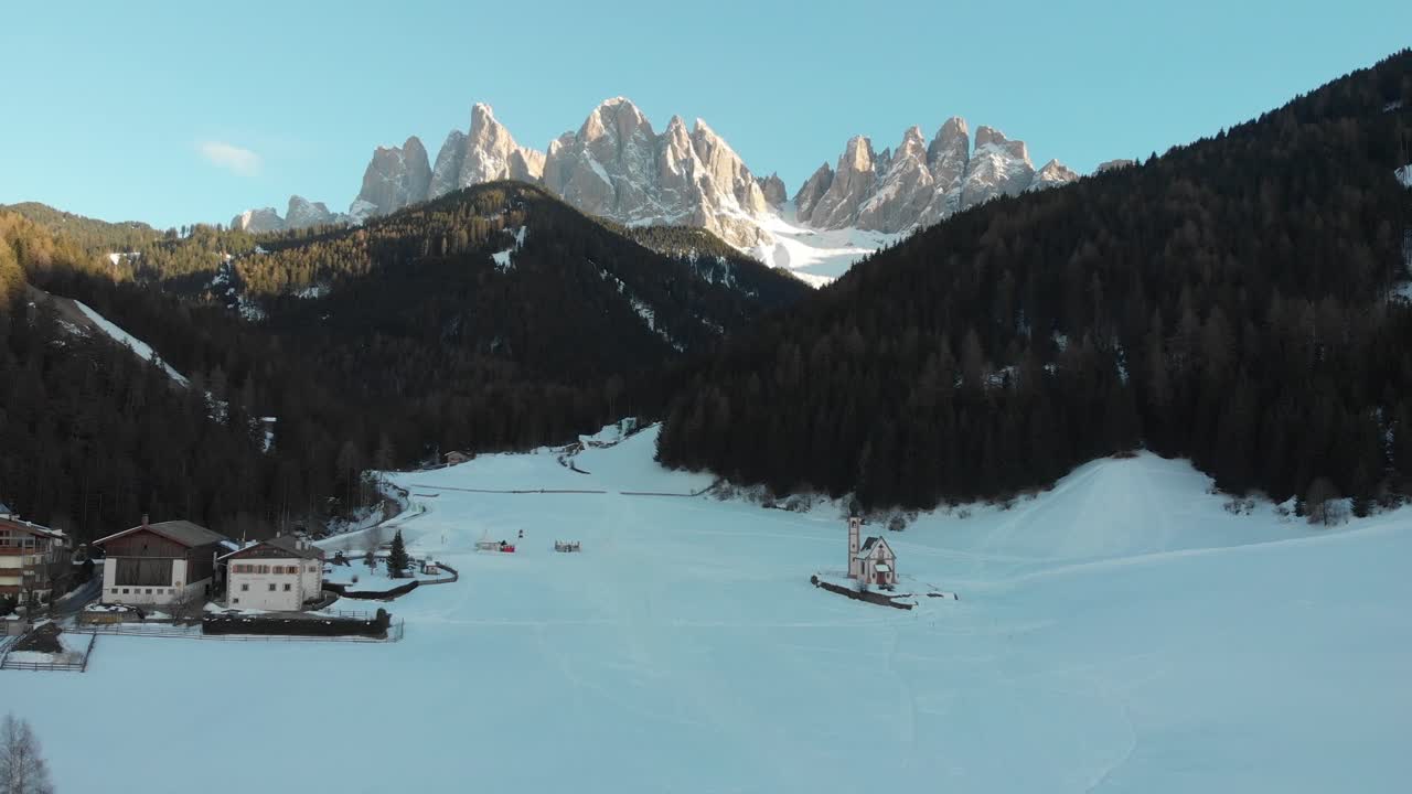 Aerial drone shot of Odle-Dolomites at sunset from Funes Tal with the famous St. John small church in snowy field, Val di Funes, Southyrol