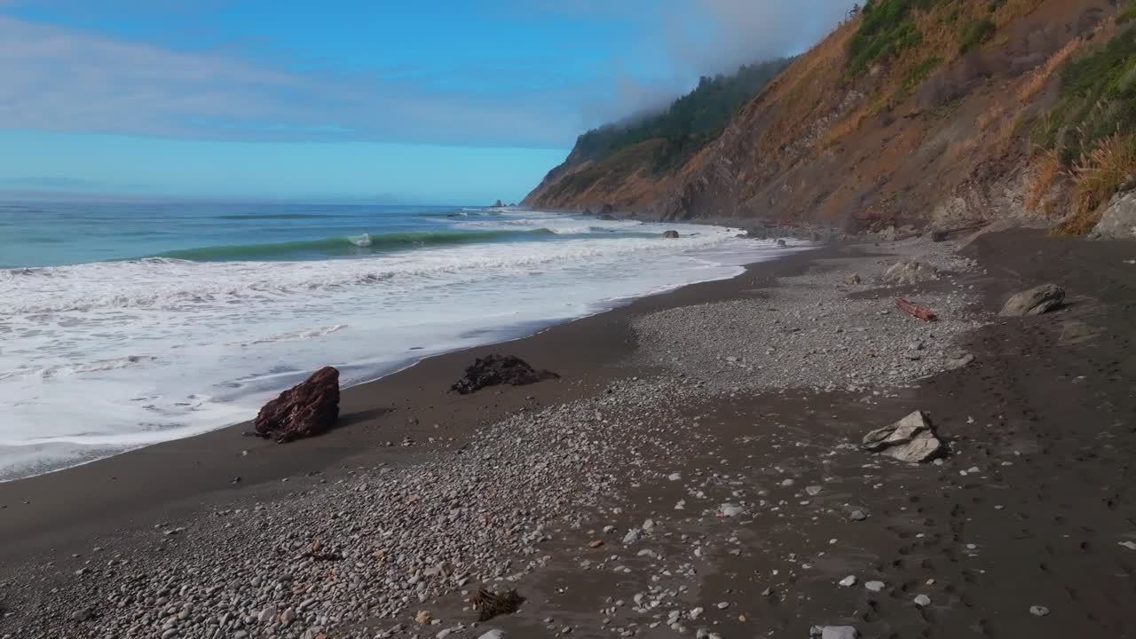 Waves crashing surf black sand rugged coastline sunny morning blue sky mist fog layer USAL Beach Campground Lost Coast Trail California aerial drone PNW boulders rocks mountainside circle left motion