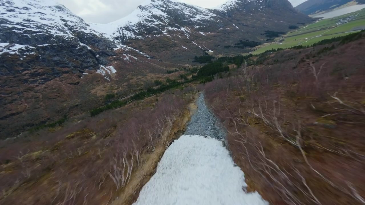 Rapid forward push FPV drone shot descending a Norwegian alpine mountain slope toward a valley with riverbed and forest.