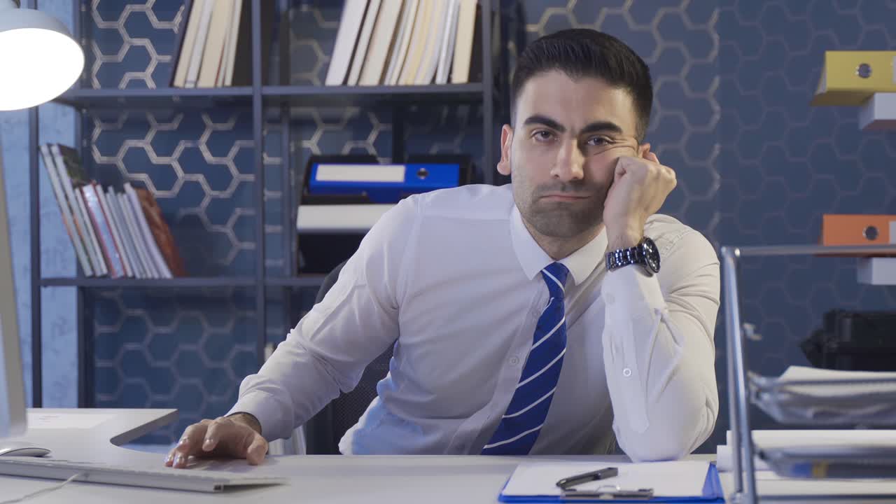 사무실 직원이 피곤하고 지친 채로 카메라를 쳐다보고 있습니다.