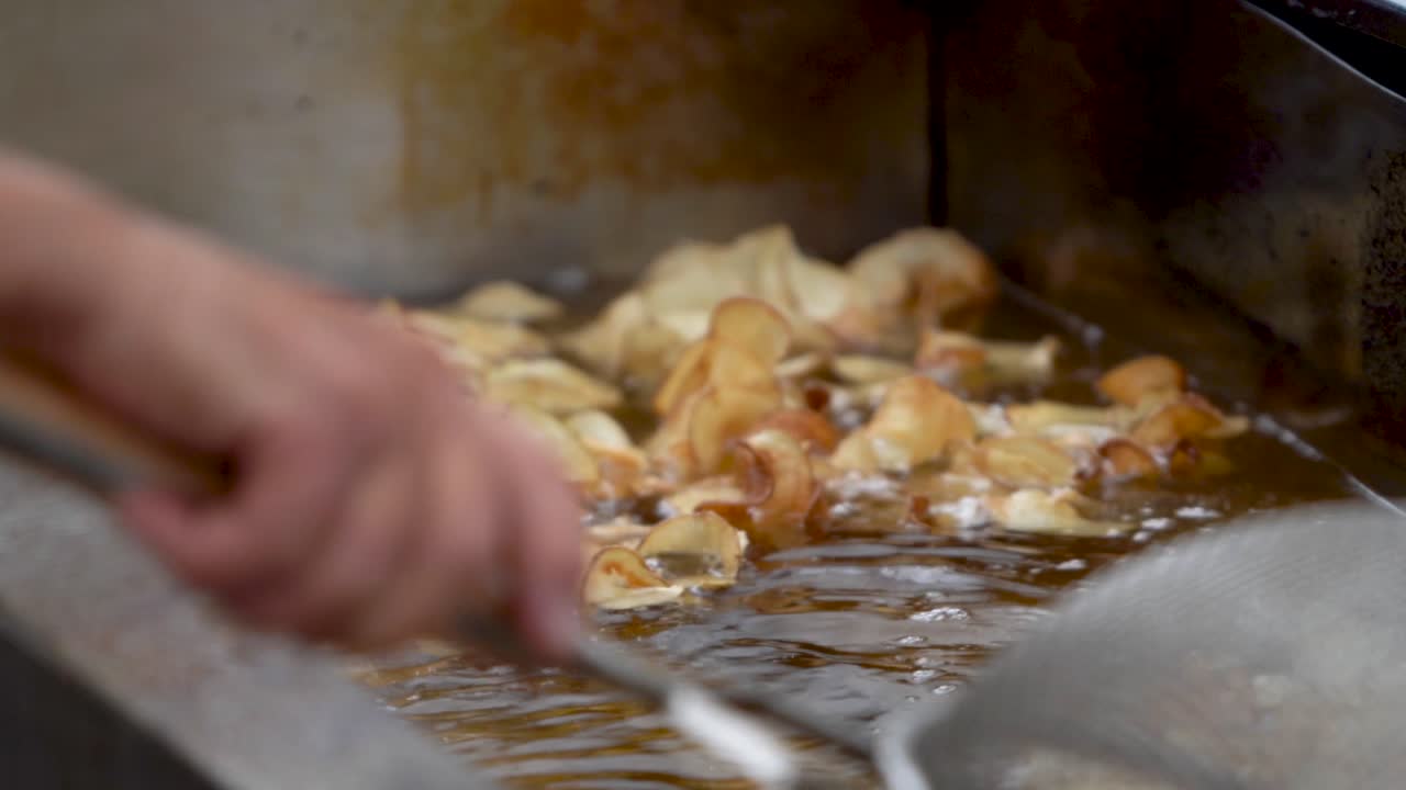 뜨거운 기름 프라이어에서 곱슬튀김을 담그는 스트레이너의 근접 촬영