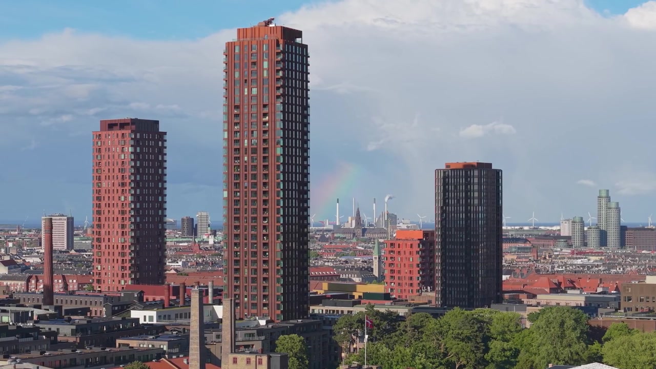 Riprese aeree che sorvolano Copenaghen mentre un vivido arcobaleno emerge dietro gli edifici della città, combinando cieli colorati, architettura urbana e luce solare intensa