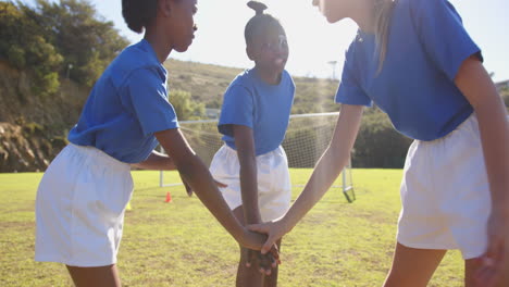 in school, girls in sports uniforms joining hands on soccer field