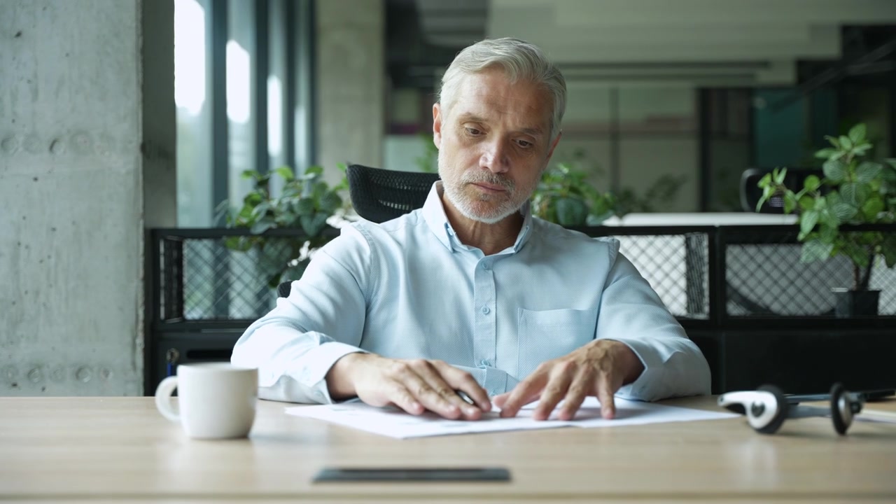 Mature Businessman Reviewing Documents at His Desk in a Modern Office