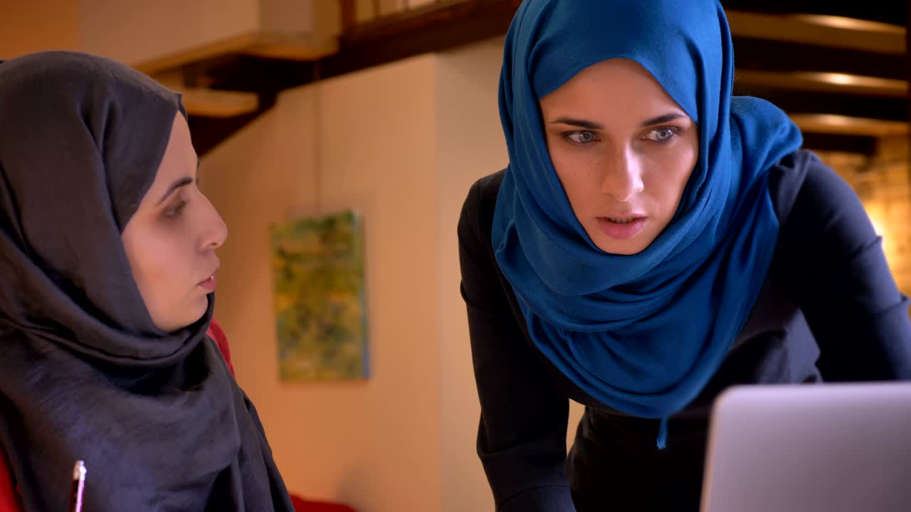 ヒジャブを着た2人の若いアラビア人女性オフィスワーカーがグラフ上のデータについて議論しているクローズアップ撮影