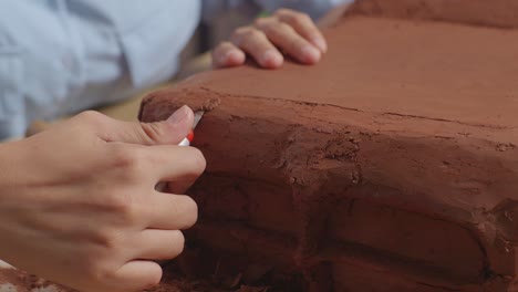 close up of woman automotive designer's hands using rake or wire to create details in the sculpture of car clay in the studio