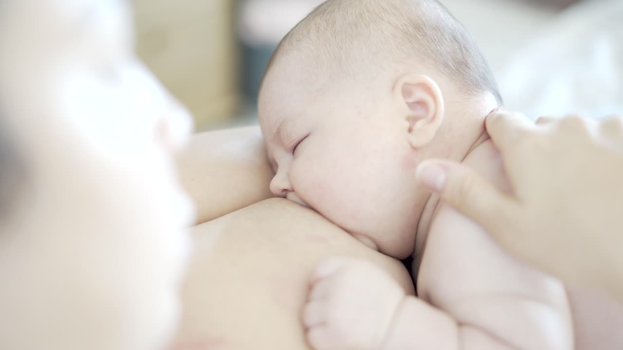 Mother caressing her 2-month-old baby while breastfeeding skin-to-skin