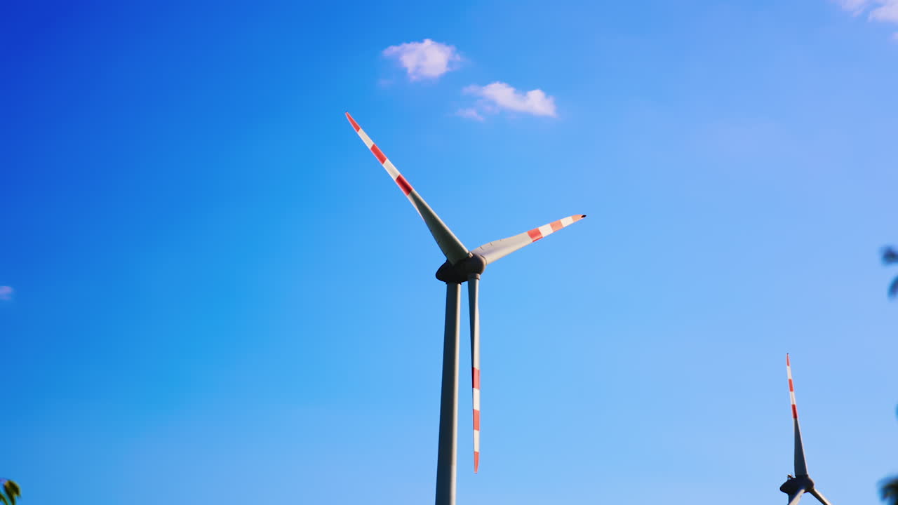 Windmill blades rotating slowly. Low angle view at the wind turbine at the backdrop of blue sky.