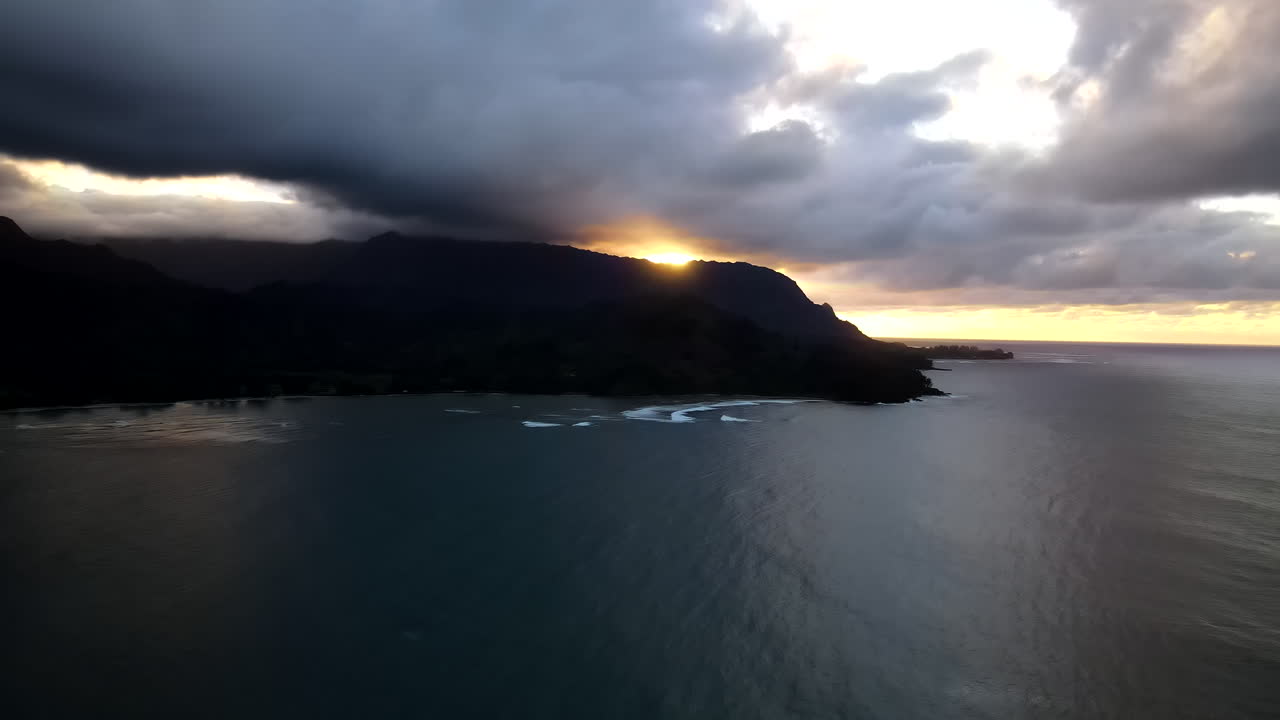 alto zoom aéreo hacia la puesta de sol sobre oscura malhumorada, nublada bahía de hanalei