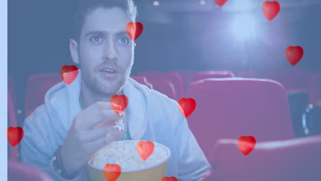 Animation-of-heart-icons-over-caucasian-man-eating-popcorn-in-cinema